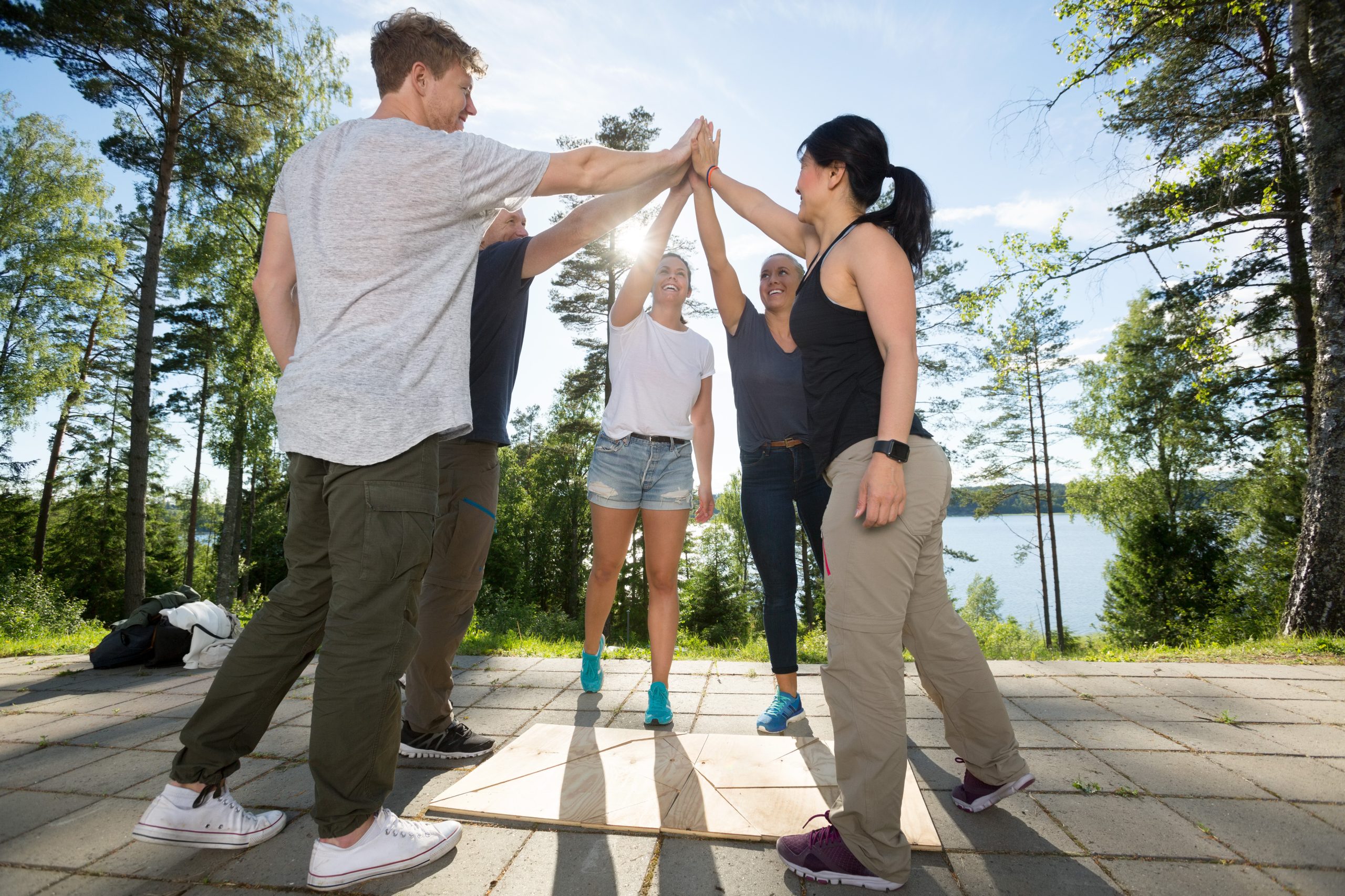 Male and female friends giving high-five after solving wooden plank puzzle on patio in forest