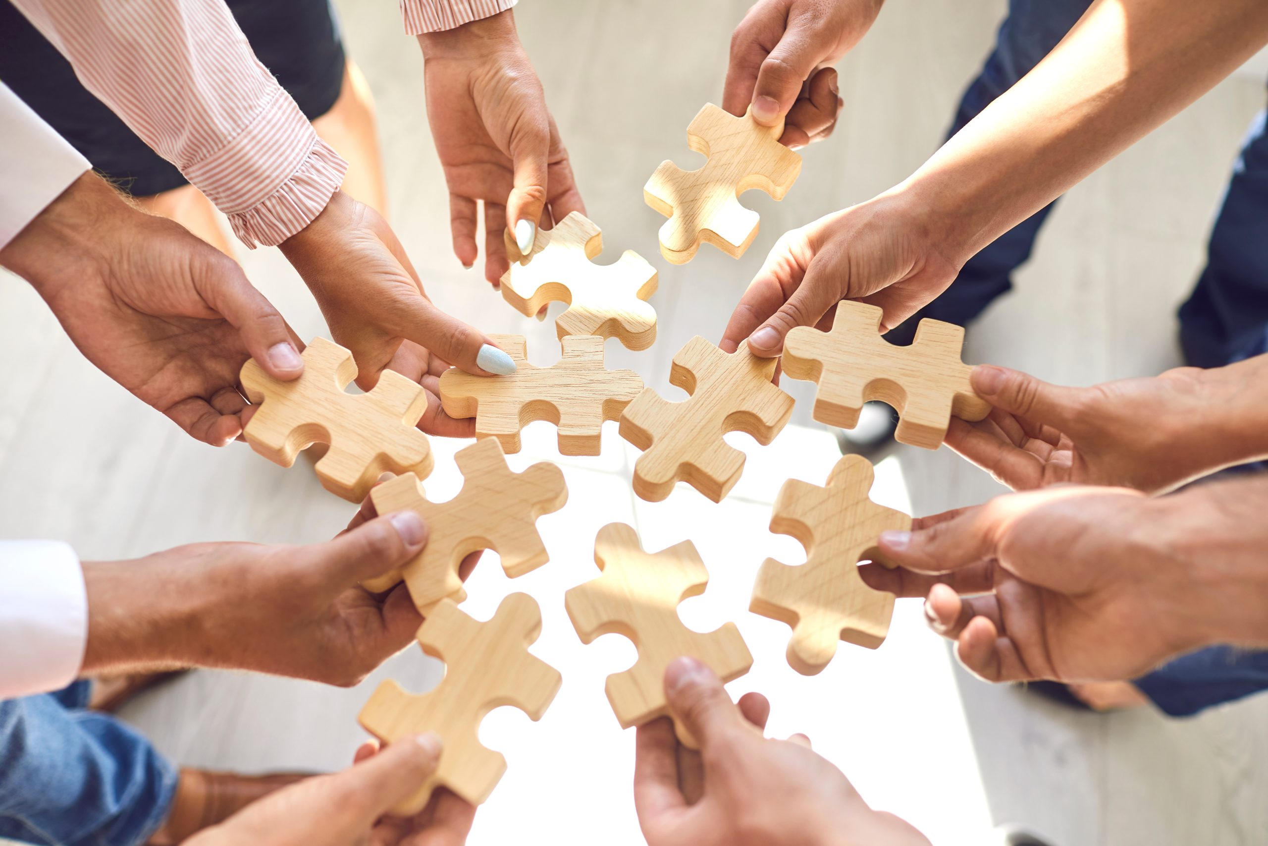 Close up of company workers finding solution in corporate work meeting. Cropped office employees learning to collaborate and playing with pieces of jigsaw puzzle during team building activity