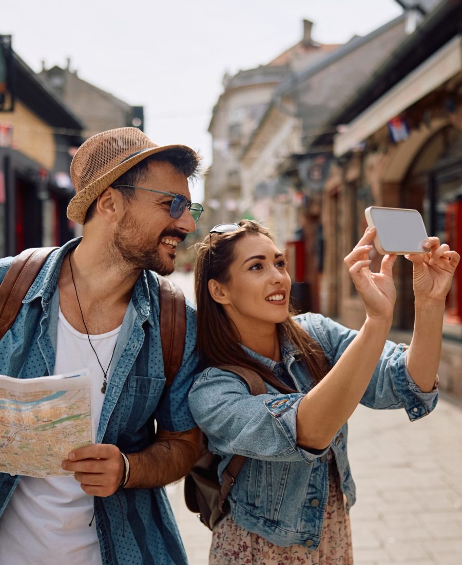 Happy tourist couple taking selfie while exploring city. Happy woman and her boyfriend taking selfie with cell phone while traveling together.
